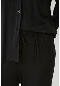 Un ensemble de détente noir comprenant un haut à boutons avec une texture douce et une coupe ample, associé à un pantalon à taille élastique pour plus de confort.