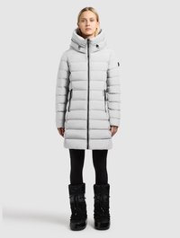 Light grey puffer coat with a high collar, zip closure, and black hardware. Worn over black leggings and black insulated boots.