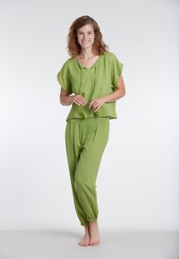 Set di abbigliamento da casa verde chiaro composto da una maglietta a maniche corte con scollatura a V e cordino, abbinata a pantaloni a gamba tapered con vita elasticizzata. Texture morbida.