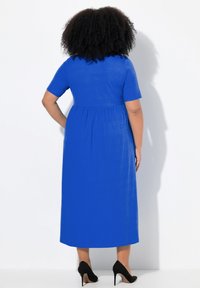 Vestido midi azul hecho de una tela ligera, con mangas cortas, cintura fruncida y un diseño liso y sencillo. Se muestran tacones altos negros.
