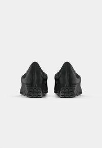 Black sneakers with a smooth leather finish, elongated silhouette, and textured rubber soles. Features a minimalist design without logos.
