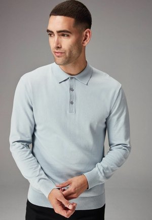 Polo albastru deschis cu mânecă lungă, guler, închidere cu trei nasturi în față, manșete ribbate și material texturat. Design simplu și modern.
