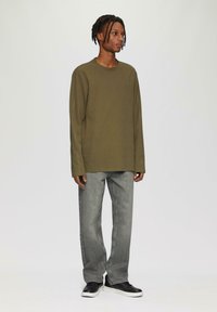 Olijfgroene langemouwen shirt met ribbelstructuur, gecombineerd met lichtgrijze rechte jeans en zwarte sneakers met witte zolen.