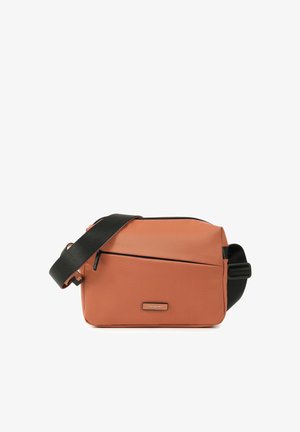 Sac bandoulière rectangulaire couleur rouille avec sangle noire réglable, poche avant zippée et petite étiquette de marque à l'avant.