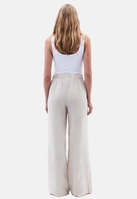 Pantalon large en lin beige avec une taille élastique, texture lisse et coupe décontractée, associé à un débardeur blanc ajusté.