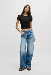 Svart kortärmad topp, matchad med ljusblå vida jeans med blekta detaljer och stora sidofickor. Svarta sandaler.