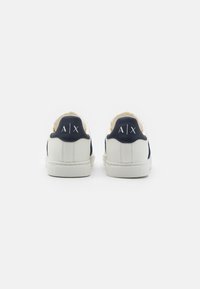 Sneakers bianchi in pelle con accenti blu navy, dotati di suola in gomma, lacci piatti e logo impresso sul tallone. Texture liscia.
