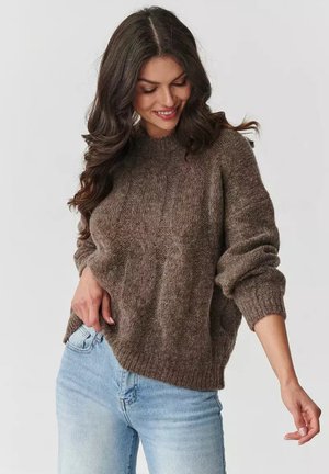 Brązowy sweter dzianinowy z okrągłym dekoltem i prążkowanym wzorem, z długimi rękawami i fakturowanym wzorem. Połączony z jasnoniebieskimi dżinsami. Miękki, przytulny materiał.