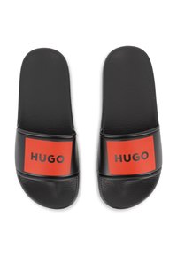 Μαύρα σανδάλια με λουρί, με υφή στο πέλμα, διαθέτουν έντονη κόκκινη ορθογώνια ταινία με την επιγραφή "HUGO" σε μαύρο κείμενο. Σχεδίαση με επίπεδη σόλα.