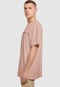 Kortærmet, oversized t-shirt i lys rosa bomuld med rund hals og sort trykt tekst på fronten. Glat tekstur, afslappet pasform.