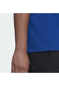 Kungablå bomull T-shirt med rund halsringning, korta ärmar och rak fåll, kombinerad med svarta byxor. Synliga sömnadsdetaljer.