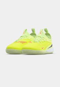 Neonowo-żółte buty sportowe z teksturowaną cholewką, kontrastowymi czerwonymi akcentami i elastyczną gumową podeszwą; wyposażone w pasek z tyłu ułatwiający zakładanie.