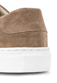 Brązowe zamszowe sneakersy z zaokrąglonym tyłem, białą gumową podeszwą i teksturowanymi akcentami. Gładka powierzchnia z chwościkami wzdłuż krawędzi.