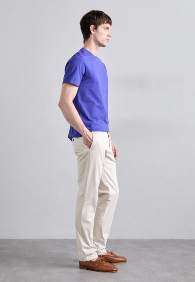 Purple cotton t-shirt, short sleeves, paired with cream-colored straight-leg trousers. Brown leather boat shoes with laces.