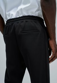 Pantalones deportivos negros con cinturilla elástica, que cuentan con dos bolsillos traseros insetados, textura suave y corte ajustado.