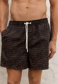 Svarta badshorts med rutsystem, dragsko i midjan och ett lätt tyg. Shortsen har fickor och en avslappnad passform.