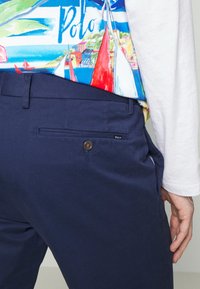 Námořnické modré bavlněné chinos kalhoty s kapsou na zadní straně na knoflíček a s logem značky, spárované s košilí s jasným vzorem.