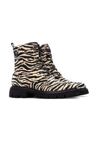 Botas de altura hasta el tobillo con un patrón de cebra, hechas de un material texturizado similar al pelo. Cuentan con cordones negros, una suela negra robusta y ojales dorados.