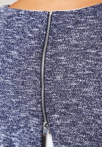 Marinblått texturerat tyg med en silverfärgad metalldragkedja som löper ner längs mitt bak. Tyget har ett subtilt prickigt mönster.