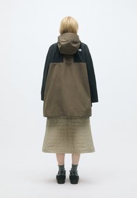 Brūns un melns apgāzts mētelis ar slāņu dizainu. Zem tā ir pītā gaiši zaļa svārku daļa. Melnas kurpes un pelēkas zeķes noslēdz apģērbu.