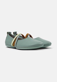 Zapatos de cuero verde claro con punta afilada, que cuentan con correas elásticas marrones y amarillas en la parte superior, y una suela plana.