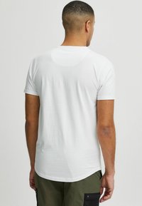 Camiseta blanca de manga corta con cuello redondo. Textura suave y corte relajado. Largura de la parte trasera ligeramente más larga y diseño minimalista.