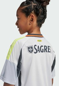 Vit fotbollsdräkt med svarta och grå detaljer, med gula ränder på axlarna och varumärket "SAGRES" på baksidan.