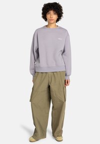 Sudadera de cuello redondo en color lila con puños y dobladillo acanalados, combinada con pantalones cargo verde oliva que tienen bolsillos laterales. Tejido de algodón suave con un ajuste relajado.