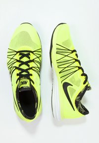 Dvojice jasně žlutých běžeckých bot Nike s černými tkaničkami a logem swoosh, jedna zobrazená z vrchu a druhá z boku.