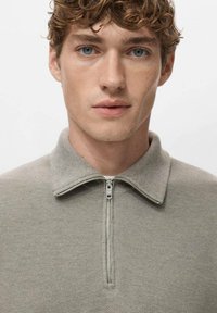 Maglione grigio chiaro con zip e colletto, realizzato in tessuto strutturato. Design semplice e pulito che mette in risalto il motivo a maglia e i dettagli sottili.