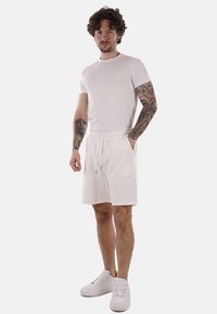 T-shirt bianca e pantaloni corti bianchi abbinati, realizzati in tessuto leggero con vita elastica e cordoncino. Presenta un design semplice e una vestibilità casual.