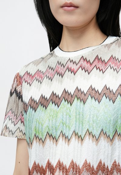 Īsroku džemperītis ar daudzkrāsainiem zigzaga rakstiem sarkanā, brūnā, zaļā un baltā krāsā. Raksturo ribota balta apkakle un maiga tekstūra.