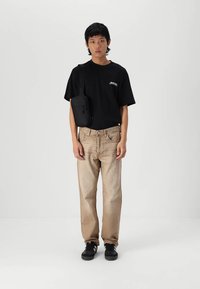 Zwart t-shirt met korte mouwen en een logo, lichtbeige denim jeans, zwarte sneakers en een kleine zwarte crossbody tas.