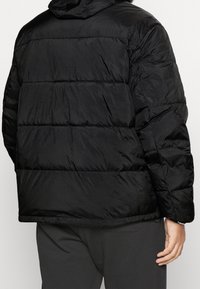 Černá prošívaná péřová bunda s kapucí a elastickými manžetami. Materiál je hladký, lehký a voděodolný.