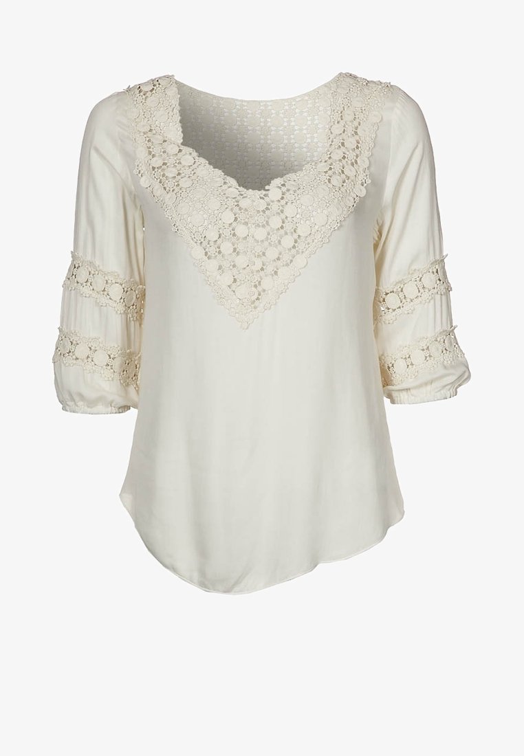 Blouse crème avec décolleté en V en dentelle et bandes en dentelle sur les manches bouffantes mi-longues, avec un ourlet arrondi.