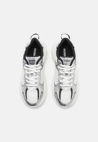 Zapatillas plateadas y blancas con parte superior de malla y cuero, puntera redonda, acentos negros y cordones blancos. Presenta una lengüeta de marca.