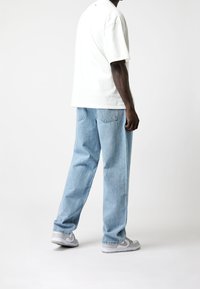 Witte oversized t-shirt, lichtblauwe straight-leg jeans en grijze sneakers. Kenmerken zijn het casual ontwerp en de ontspannen pasvorm.