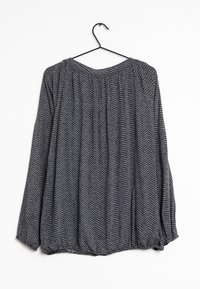 Blouse à manches longues avec un motif en chevron noir et gris, dotée d'un col froncé et d'une coupe ample, suspendue à un crochet noir.