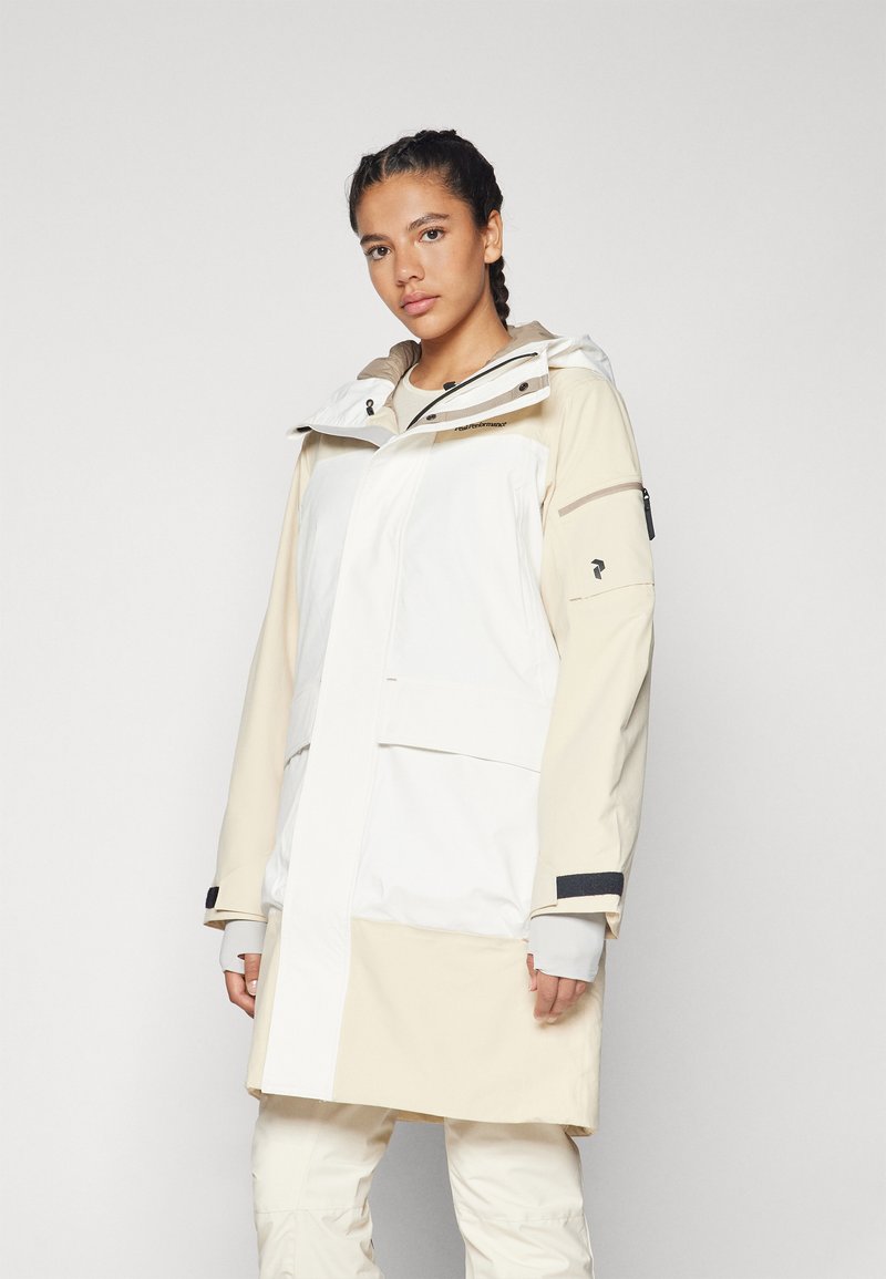 Lightweight, two-tone jacket in white and beige with a hood, zip and button closure, adjustable cuffs, and multiple pockets. Made of water-resistant material.