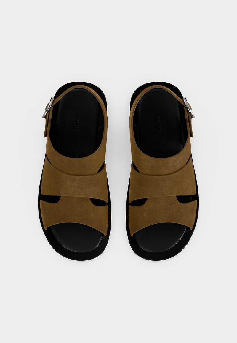 Par de sandalias de cuero marrón con suelas negras, con tiras anchas y cierres de hebilla de metal, vistas desde arriba sobre un fondo blanco.