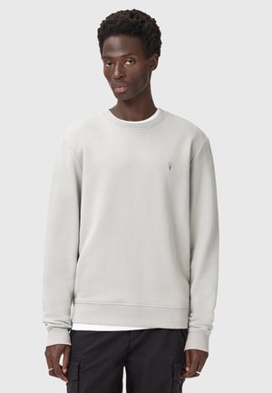 Lys grå sweatshirt med lange ærmer og rund halsudskæring. Har et lille logo på brystet. Blødt stof med en glat tekstur.