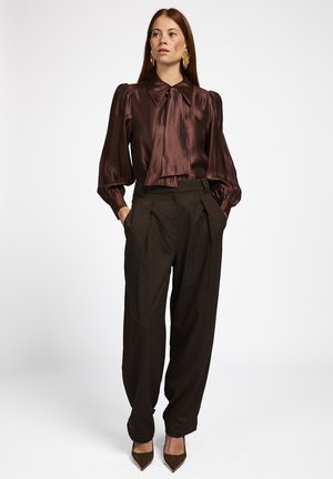 Bruine satijnen blouse met een grote kraag en een gestrikt detail, gecombineerd met hooggetailleerde bruine plooibroek en spitse bruine hakken.