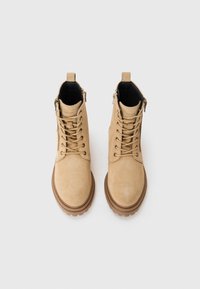 Bottines en daim tan, avec bouts ronds, fermeture à lacets à l'avant et fermetures éclair sur les côtés. Présentent une semelle en caoutchouc et un design robuste.