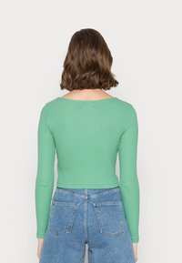 Top verde às riscas de mangas longas com decote redondo, design cropped e tecido texturizado, combinado com calções de ganga azuis de cintura alta.