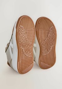 Baskets avec une semelle en caoutchouc présentant un motif en zigzag texturé. Partie supérieure en matériau synthétique beige avec des accents blancs.
