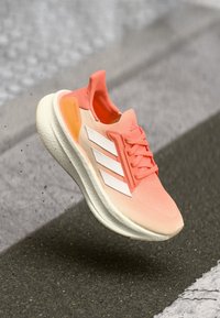 Adidas løbesko i gradient fersken og hvid, med en åndbar tekstiloverdel, struktureret sål og tre karakteristiske hvide striber.