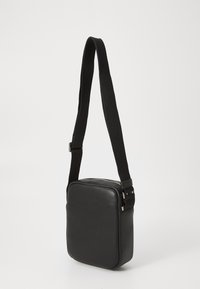 Borsa a tracolla sintetica nera con forma quadrata, texture liscia, tracolla regolabile in tessuto e dettagli in metallo argentato. Chiusura con cerniera sulla parte superiore.