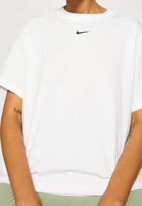 Vit bomulls-t-shirt med rund halsringning och korta ärmar. Svart Nike-logotyp centrerad på bröstet. Mjuk textur, ledig passform.