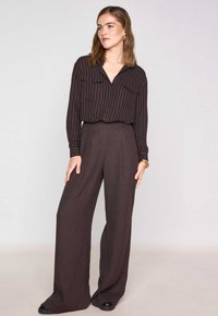 Camicia con bottoni e righe verticali in colori scuri, abbinata a pantaloni scuri a vita alta e gamba larga. Tessuto liscio, design minimalista.