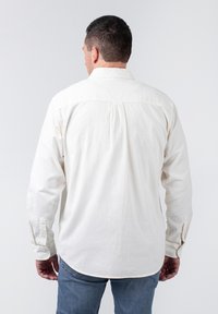 Langärmliges, kragenloses Hemd aus einfarbigem Creme, aus Baumwollstoff. Mit Knopfmanschetten und Rückenpasse. Die Rückansicht zeigt eine lockere Passform.